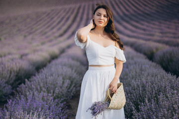 Woman wearing white dress posing in lavender field holding wicker basket