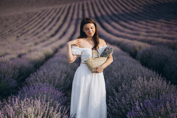 Woman wearing white dress holding wicker basket posing in lavender field