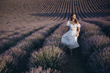 Woman wearing white dress walking in lavender field at sunset