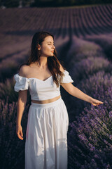 Young woman in white dress walking in lavender field at sunset