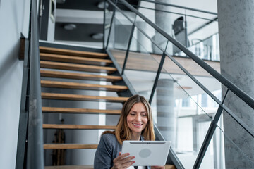 Businesswoman smiling and using digital tablet on stairs in modern office