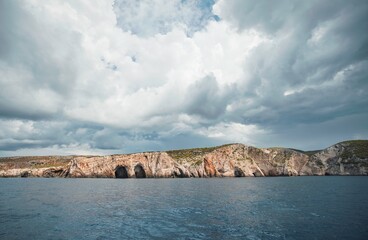 A boat tour moves along the Ionian Sea near Zakynthos. Caves are visible in the rocky coastline as...