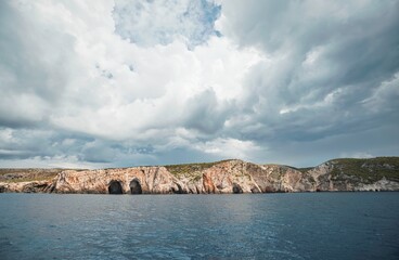 Dramatic skies loom over the Ionian Sea as a boat approaches the rocky coastline of Zakynthos....