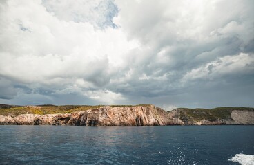 Dramatic cliffs meet the Ionian Sea under a sky heavy with storm clouds near Zakynthos. The boat...