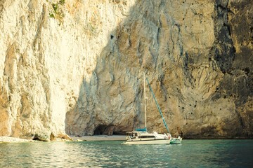 A white sailboat rests near a small sandy beach nestled between towering, light-colored cliffs on...