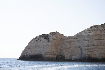 A majestic rock formation towers above the turquoise waters near Zakynthos. Layers of stone etched...