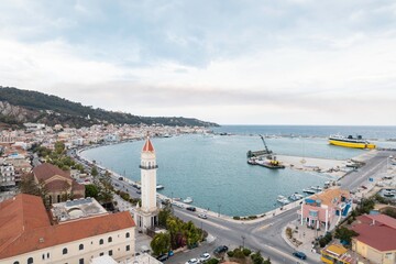 From above, a coastal city vista showcases a prominent bell tower near a harbor where ferries and...