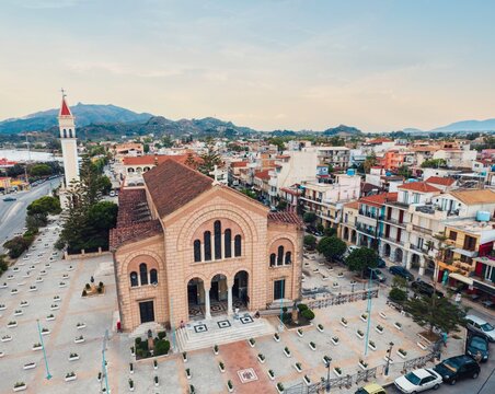 An elevated perspective shows Saint Dionysios Church standing proudly in its square, part of the sprawling town of Zakynthos, with mountains in the distance under a serene sky