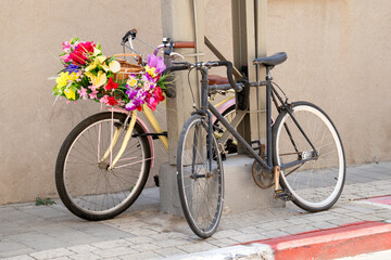 Two bicycles parked on a sidewalk, one decorated with colorful artificial flowers in a basket, creating a charming vintage street scene.