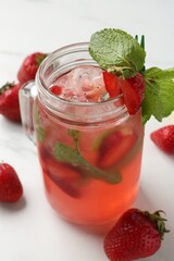 Refreshing drink with strawberries, ice and mint on white table, closeup