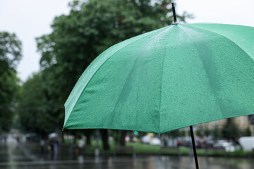 Green umbrella under heavy rain outdoors, closeup