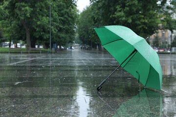 Green umbrella under heavy rain outdoors, space for text