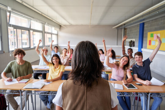 Multiethnic high school students raising hands to answer teacher's question in classroom. Image with copy space.