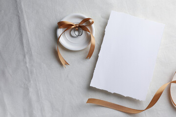 Wedding invitation card, silver rings and ribbon on white cloth, flat lay. Space for text