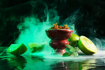 Hookah bowl with limes, mint and smoke on black table, closeup