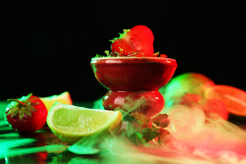 Hookah bowl with limes, strawberries, mint and smoke on black table, closeup