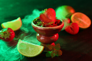 Hookah bowl with limes, strawberries, mint and smoke on black table, closeup