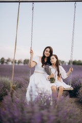 Mother and daughter swinging and enjoying beautiful lavender field