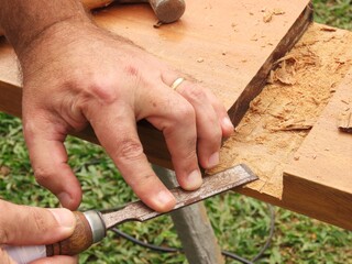 Man hands using a chisel to make cut in a wood plank. Closeup of man hands using a tool for carving...