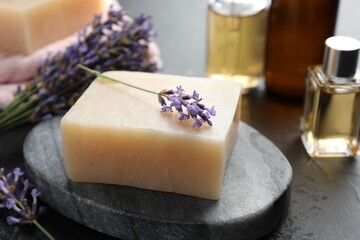 Aromatic soap bar and lavender flowers on dark textured table, closeup