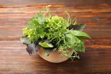 Mortar with different aromatic herbs on wooden table, closeup