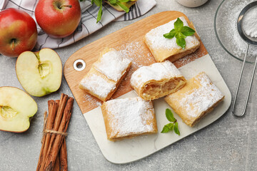 Pieces of tasty apple strudel with powdered sugar and mint on light grey table, flat lay