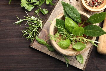 Mortar with different fresh herbs and peppercorns on wooden table, flat lay