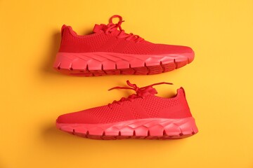 Pair of red sneakers on orange background, flat lay