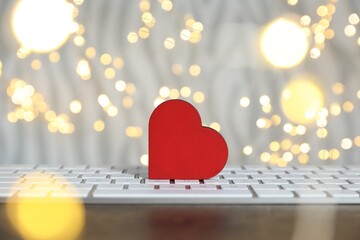 Decorative heart and computer keyboard on table against blurred lights, bokeh effect. Online dating...