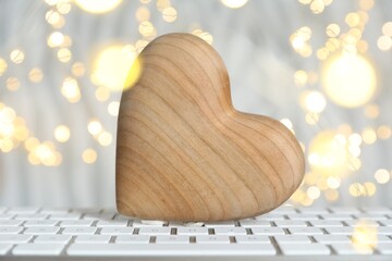 Online dating site. Wooden heart on computer keyboard against blurred lights, closeup. Bokeh effect