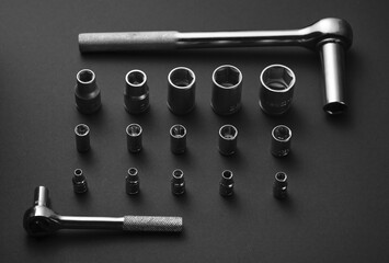 A silver ratchet wrench surrounded by a collection of interchangeable socket adapters.