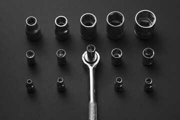 A chrome socket wrench and adapters are arranged on a dark gray surface