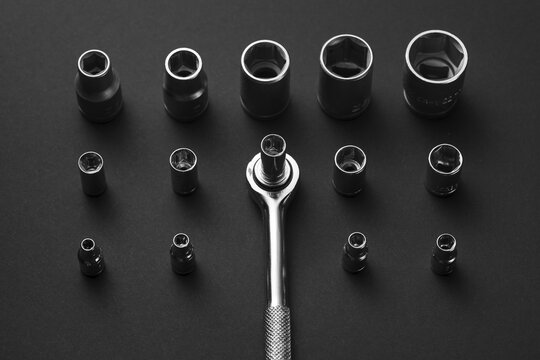 A chrome socket wrench and adapters are arranged on a dark gray surface