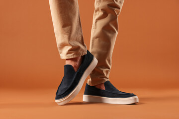 Man wearing pair of dark blue shoes on brown background, closeup