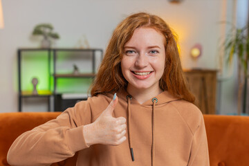 Portrait of excited smiling Caucasian woman looking approvingly at camera showing double thumbs up,...