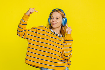Happy joyful Caucasian woman in blouse listening music on headphones and dancing disco fooling...