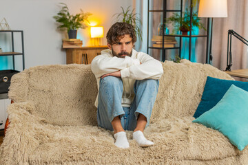 Sad frustrated young Indian man sitting at home looks pensive thinks over lonely life or problems,...