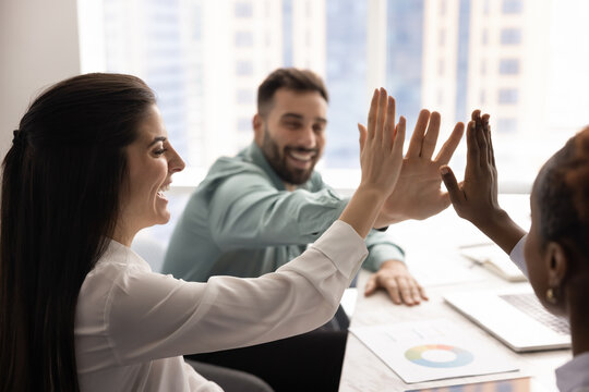 Three happy teammates, staff members stacking their palms together in high-five gesture, symbolizing effective teamwork completion, celebrate shared success and collective achievement. Synergy, unity