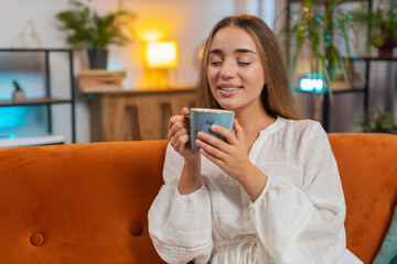 Portrait of smiling young woman drinking cup of warm coffee or herbal tea in the morning. Caucasian...