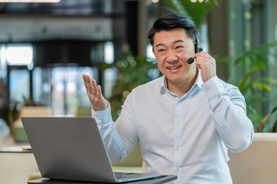 Chinese businessman wearing headset, call center or support service operator helpline, having talk with client or colleague communication support in office lobby. Guy in shirt sits on couch in hotel. - Powered by Adobe