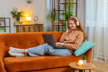 Happy relaxed overjoyed Caucasian redhead woman in wireless headphones sitting on home sofa...