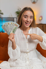 Successful rich Caucasian woman holding waving dollar bill money fan sitting on couch at home room....