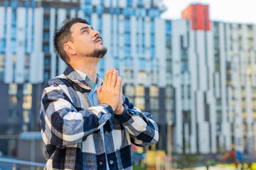 Mature Caucasian man tourist male face standing in downtown city street folding palms praying...