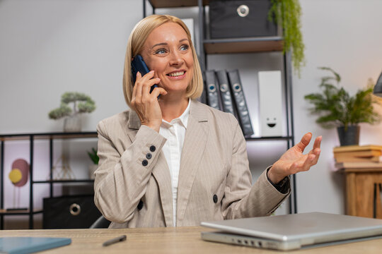 Mature businesswoman freelancer answering to client on mobile phone call, using smartphone. Conversation. Caucasian middle-aged woman working online remote distance job, talking at home office desk.