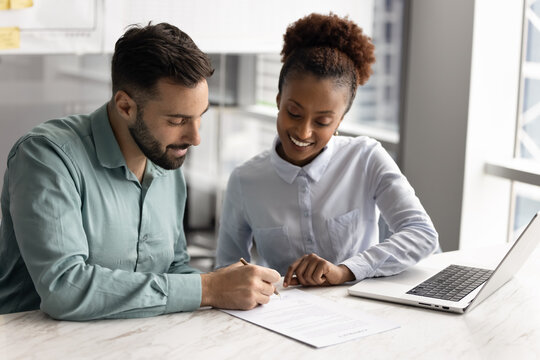 Man signing contract during meeting with young professional African woman, accepting job offer, confirming new employment and responsibilities, finalizing business partnership, closing sales agreement