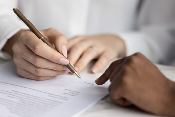 Close up of womans hands on paper document, bank advisor pointing to area to sign, client holds pen...