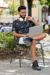 Indian bearded man with wireless headphones around neck working online distant job with laptop...