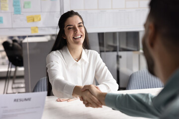 Smiling young Hispanic female vacancy applicant, seeker shaking hands with male hr manager,...