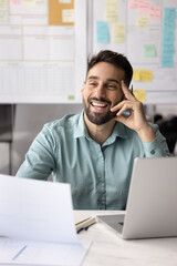 Laughing businessman sitting at desk with laptop, holds papers feeling satisfied with his work or...