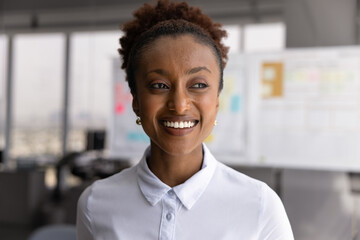 Head shot portrait of African businesswoman, sales manager looks aside with joyful, contented...